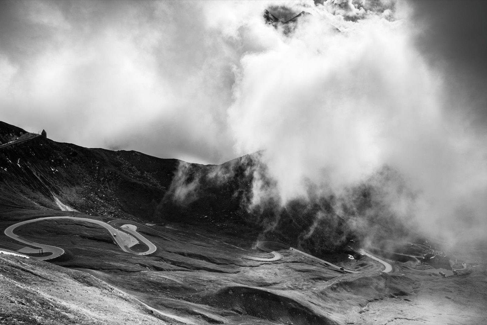 Route de col alpine sous les nuages, noir et blanc